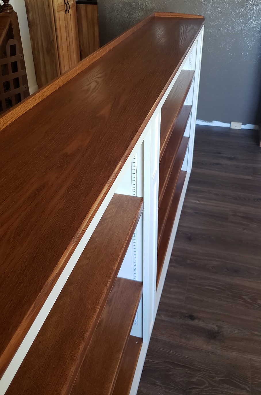 Long stained oak top on white built in bookshelf in front of brown wall