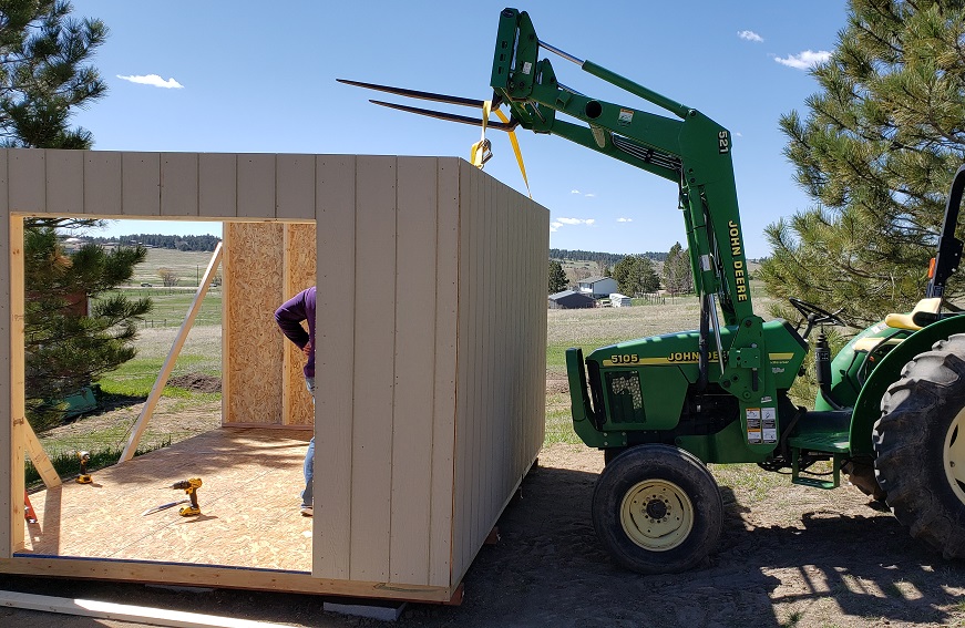 Wall being installed on a shed held up with a John Deere 5105 tractor and 521 loader