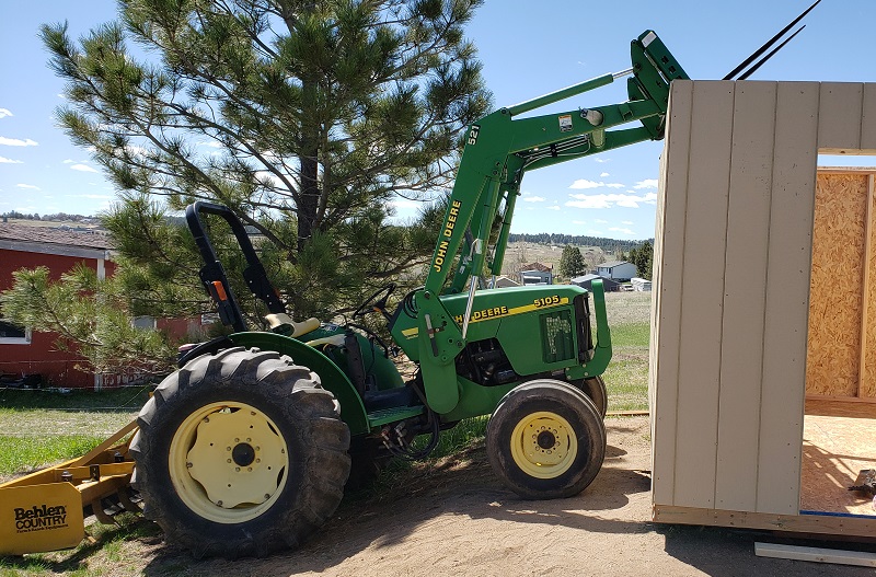 Wall being installed on a shed held up with a John Deere 5105 tractor and 521 loader