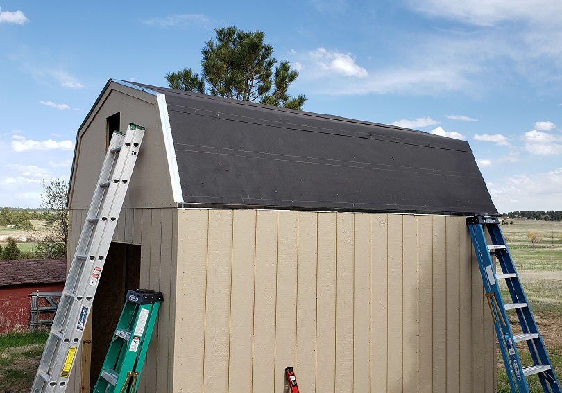 Unpainted gambrel style shed with roof drip line and tar paper installed