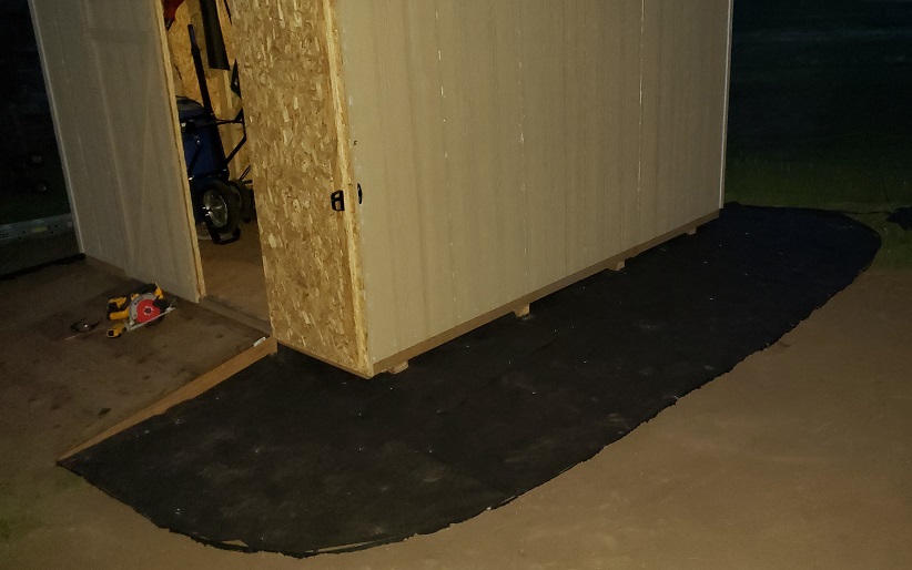 Weed barrier installed around unpainted storage shed