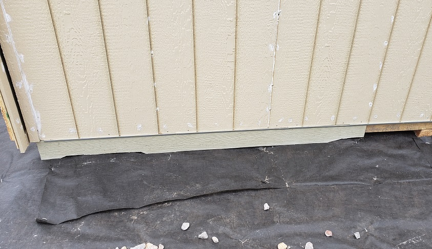 Hardie board siding installed to ground on shed in front of weed barrier