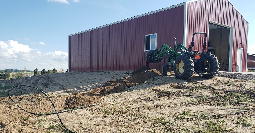 Service wire spole on John Deere 5105 521 loader in front of red pole barn