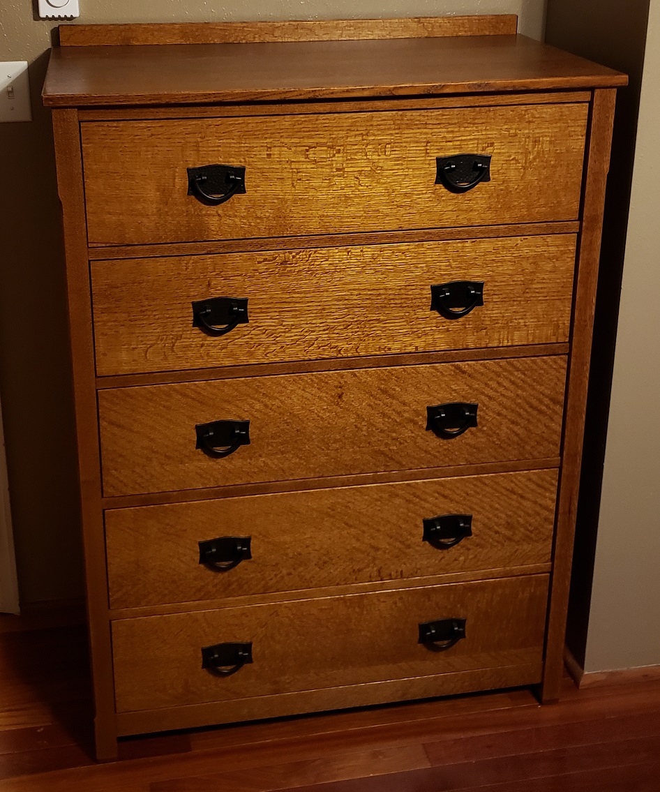 Five drawer mission style quartersawn oak dresser with black pulls in front of brown wall
