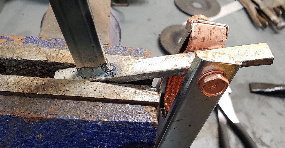 Welded metal with grounding clamp in blue bench vise